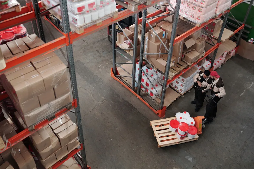 Workers managing inventory on shelves in a warehouse, viewed from above.