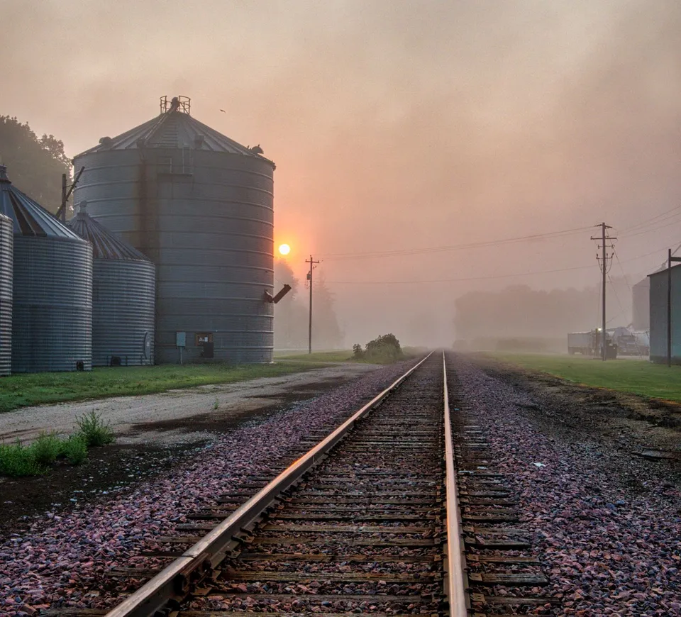 A serene foggy sunrise over railway tracks and steel silos in Utica, MN, USA.