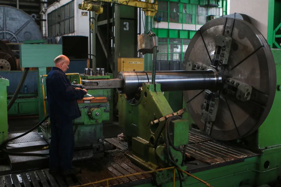 Adult male worker inspecting large machinery in an industrial factory setting.